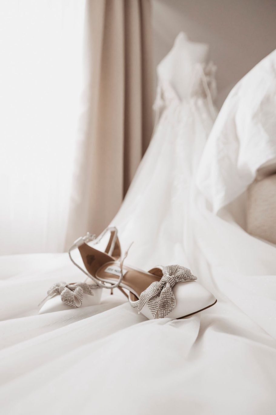 Elegante Brautschuhe liegen auf einem Bett neben einem weißen Hochzeitskleid.