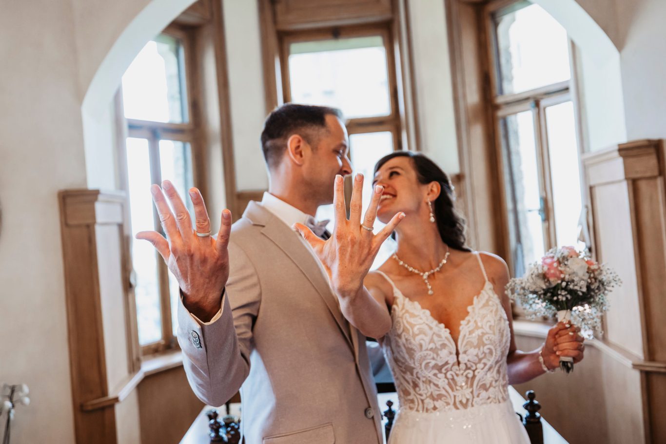 Ein Brautpaar zeigt seine Ringe und lächelt sich liebevoll an.