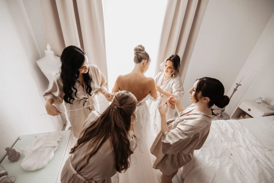 Hochzeitsfotograf Stuttgart - Eine Braut wird von vier Frauen in Bademänteln beim Ankleiden unterstützt.