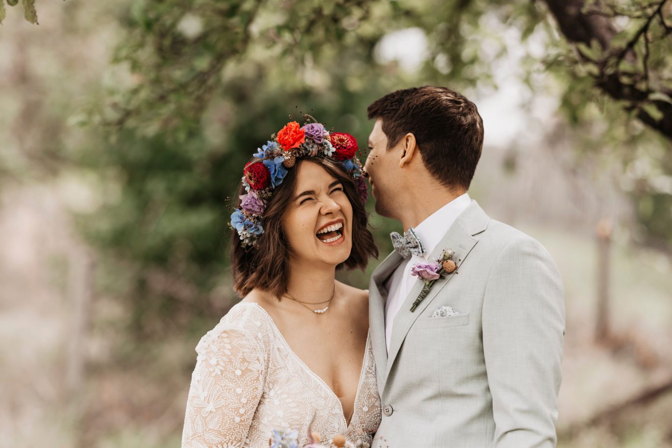 Brautpaar lacht glücklich unter Bäumen.